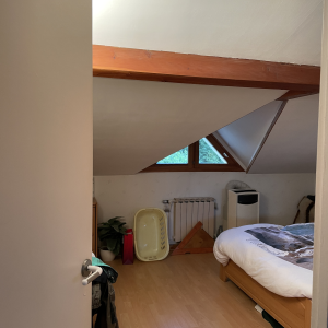 Vue d’entrée d’une chambre mansardée avec lit double, sous-pente et fenêtre triangulaire – état existant