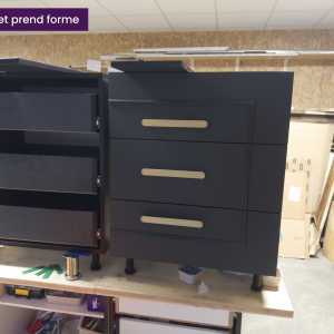 Caisson de meuble noir avec tiroirs en cours de montage, poignées dorées posées en atelier