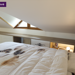 Vue de face d’un meuble bas toute longueur sous fenêtre en pente, avec niches, rangements fermés et objets déco.