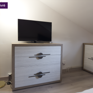 Zoom sur la commode sous pente avec TV, câbles visibles au sol, meubles coordonnés et finition bois blanchi avec poignées noires contrastantes.